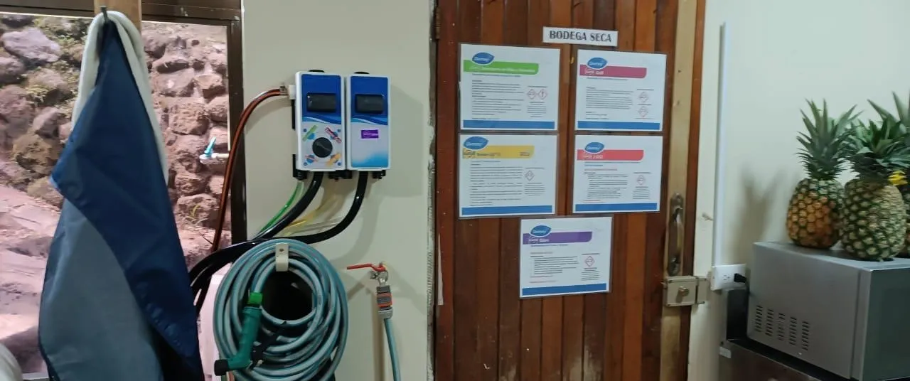 Sistema de dosificación de químicos Diversey montado en pared en una bodega de alimentos, con fichas técnicas de producto a la vista.